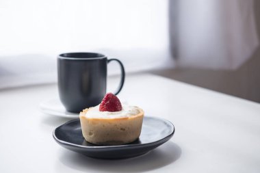 Bir çilek peynirli tart, bir fincan sıcak kahve ve kaktüs beyaz vintage ahşap masa ve perde arka planda minimalizm Cafe