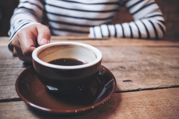 カフェでヴィンテージの木製テーブルの上のコーヒーのカップを持っている女性の手のクローズ アップ画像 — ストック写真