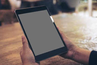 Cafe ahşap masa arka plan üzerinde siyah tablet pc ile gri boş perde holding eller mockup görüntü