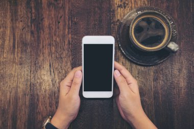 Mockup görüntü ile boş siyah perde ve sıcak kahve fincanı kafede vintage ahşap masa arka plan üzerinde beyaz cep telefonu