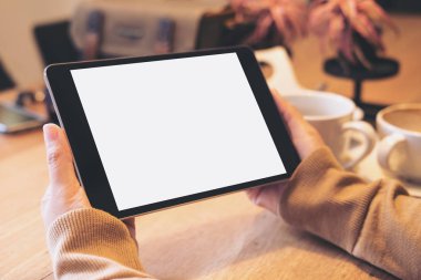 Siyah tablet pc ile kahve fincanı ahşap masa üzerinde boş beyaz ekran ile modern kafede holding eller mockup görüntü
