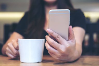 Portre resim kullanarak ve modern kafede beyaz kahve fincanı tutarken akıllı telefon arıyorum güzel bir Asyalı kadın