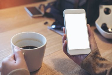 Kadının görüntüsünü mockup holding beyaz cep telefonu ile boş perde ve beyaz kahve fincanı modern loft kafede eller