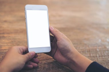 Mockup görüntü tutarak ve ahşap masa arka plan boş ekran ile beyaz cep telefonu kullanarak kadının el
