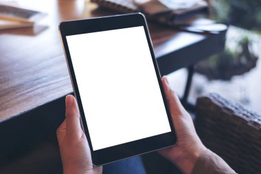 Cafe ahşap masa arka plan üzerinde siyah tablet pc ile beyaz boş perde holding eller mockup görüntü