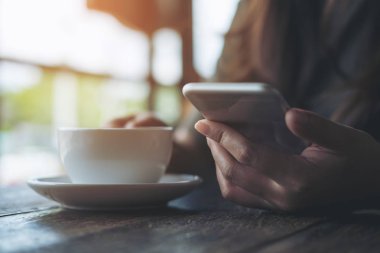 Portre resim kullanarak ve modern kafede beyaz kahve fincanı tutarak akıllı telefon arayan bir kadın