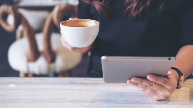 Portre resim bir kadın tutarak ve modern kafede kahve yudumlarken tablet PC'yi kullanma