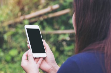 Bir kadın tutarak ve açık ve yeşil doğa arka planda boş siyah perde ile beyaz akıllı telefon kullanarak mockup görüntü
