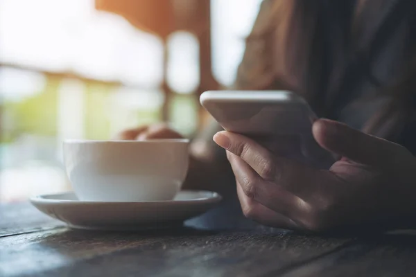 Portre resim kullanarak ve modern kafede beyaz kahve fincanı tutarak akıllı telefon arayan bir kadın