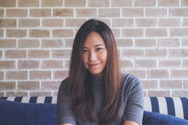 Portre portre resim gülen ile güzel bir Asya kadının iyi duygu ile kanepede oturan yüz ve relax tuğla duvar arka plan ile