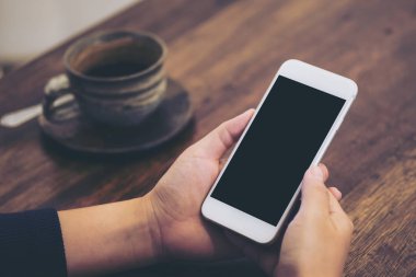 Beyaz cep telefonu ile boş siyah perde ve kahve fincanı vintage ahşap masa üzerinde tutan el mockup görüntü 