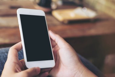 Beyaz cep telefonu ile boş siyah perde ile holding eller görüntüsünü mockup Cafe ahşap masa arka plan bulanıklık