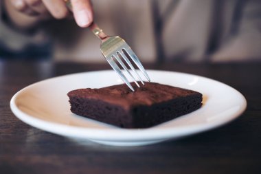 Vintage ahşap kafede beyaz tabakta çatal ile bir kadın kesme brownie kek
