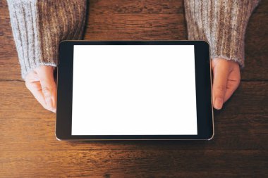 Mockup üst kadının elleri tutan ve vintage ahşap masa üzerinde siyah tablet pc boş beyaz ekran ile gösterilen görüntüsünü göster 