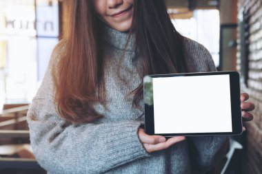 Mockup görüntüsünü tutan ve siyah tablet pc boş beyaz ekran ile modern kafede gösteren güzel bir Asyalı kadın