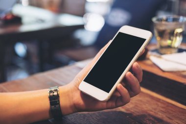 Bir kadının görüntüsünü mockup holding beyaz cep telefonu ile boş siyah perde ile çay bardağı vintage Cafe ahşap masa üzerinde eller