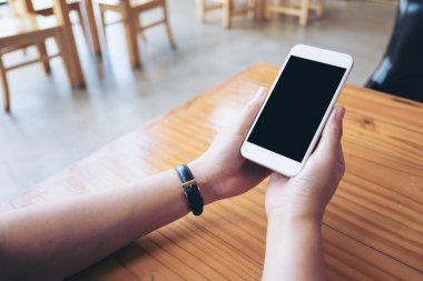 Cafe ahşap masa üzerine boş siyah perde ile beyaz cep telefonu holding eller mockup görüntü
