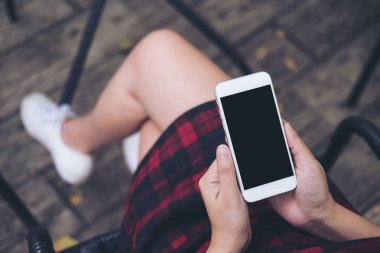 Bir kadının el vintage kafede uyluk ile ahşap zemin arka plan üzerinde beyaz cep telefonu boş siyah perde ile tutarak mockup görüntü