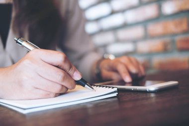 Portre resmi defter ve kullanma ve modern Cafe ahşap masa üstünde smartphone gösteren yazılı bir kadının elleri   