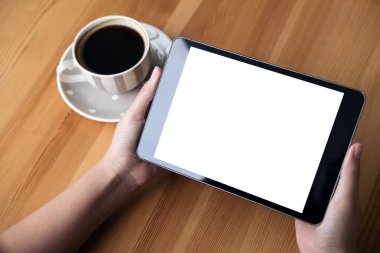 Mockup görüntü iş kadının elleri boş beyaz ekran ve ahşap masa üzerinde kahve fincanı ile siyah tablet pc kafe arka planda tutan