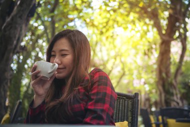 Portre portre resim güzel bir Asya kadının beyaz holding kupa ve yeşil doğa arka planda mutlu duygu ile sıcak kahve içme keyfini çıkarın