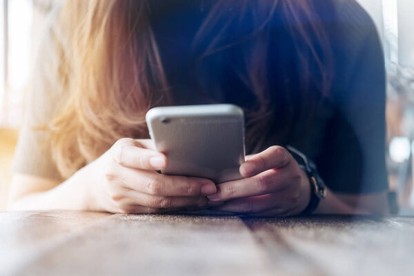 Крупный план женских рук, держащих и использующих смартфон на деревянном столе в винтажном кафе
