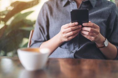 Kafe 'de elinde kahve fincanıyla cep telefonu tutan ve kullanan bir kadının yakın plan görüntüsü.