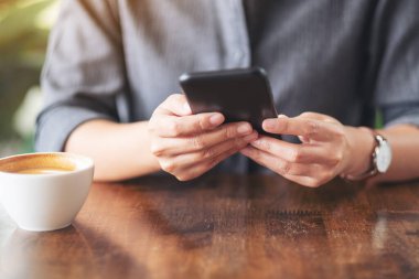 Kafe 'de elinde kahve fincanıyla cep telefonu tutan ve kullanan bir kadının yakın plan görüntüsü.