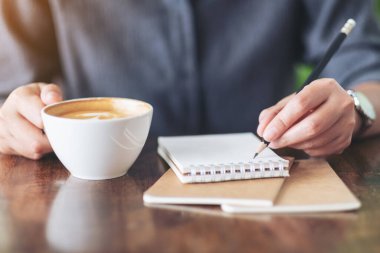 Not defteri ve kahve fincanı tutan bir kadının yakın plan görüntüsü.