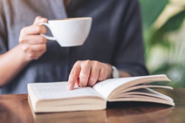 Ahşap masada kahve içerken kitap okuyup işaret eden bir kadının yakın plan resmi.