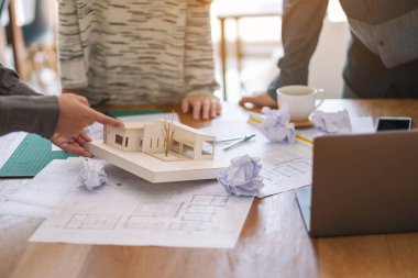 Bir grup mimar, mimarlık modeli üzerinde çalıştıktan sonra ofis masasında kağıt çizerken stresli hissediyorlar.