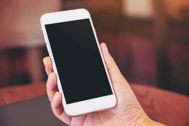 Ahşap masadaki dizüstü bilgisayarlı, boş beyaz ekranlı, siyah cep telefonlu bir kadının ellerinin görüntüsü.