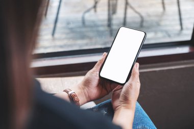 Kafedeki boş masaüstü ekran ile siyah cep telefonu tutan bir kadının görüntüsü