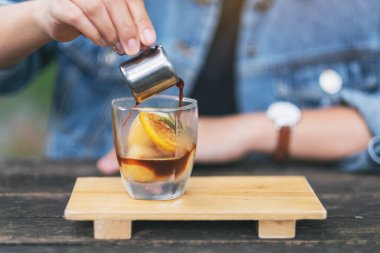 Bir kadın bir bardak buz ve limona espresso dolduruyor.