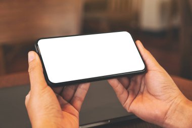 Masada dizüstü bilgisayarlı ve boş masaüstü ekranlı siyah cep telefonu tutan ellerin görüntüsü