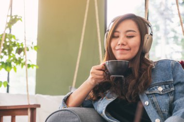 Güzel bir Asyalı kadın kahve içerken kulaklıkla müzik dinliyor. 