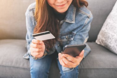 Asyalı bir kadın cep telefonundan alışveriş yapmak için kredi kartı kullanıyor.
