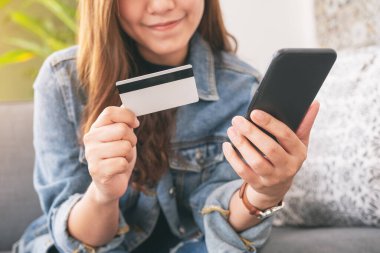 Asyalı bir kadın cep telefonundan alışveriş yapmak için kredi kartı kullanıyor.