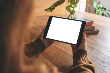 Tahta masanın üzerinde beyaz ekranlı siyah tablet tableti tutan ve kullanan bir kadının görüntüsü