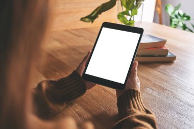 Tahta masanın üzerinde beyaz ekranlı siyah tablet tableti tutan ve kullanan bir kadının görüntüsü