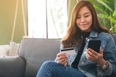 Asyalı bir kadın cep telefonundan alışveriş yapmak için kredi kartı kullanıyor.