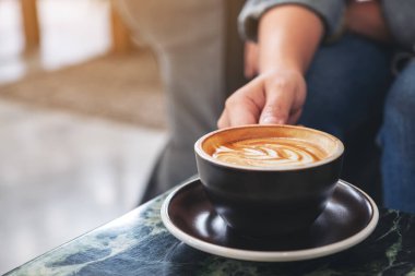Masanın üzerinde bir fincan sıcak kahve tutan bir elin yakın plan resmi.