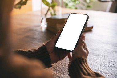 Masanın üzerinde boş masaüstü ekranı olan siyah cep telefonu tutan kadının görüntüsü.