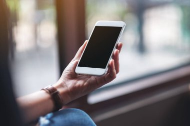 Kafede boş masaüstü ekranı olan beyaz cep telefonu tutan bir kadının görüntüsü