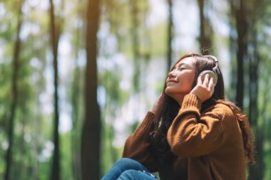 Güzel Asyalı bir kadın kulaklıkla müzik dinlemekten hoşlanır. Parkta mutlu ve rahat hisseder.