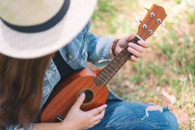 Güzel bir Asyalı kadın dışarıda oturup ukulele çalıyor.