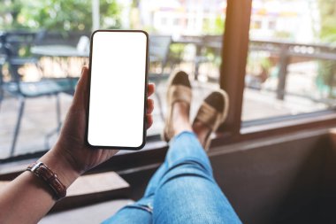 Kafede otururken elinde boş masaüstü ekran olan siyah cep telefonu tutan bir kadının görüntüsü