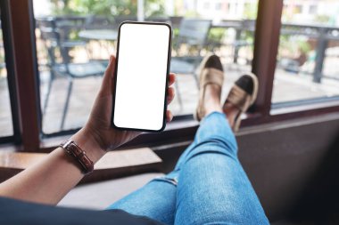 Kafede otururken elinde boş masaüstü ekran olan siyah cep telefonu tutan bir kadının görüntüsü