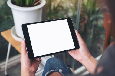 Kafede otururken elinde siyah tablet beyaz ekranlı bir kadın resmi.