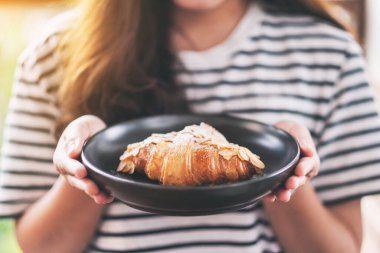 Elinde taze bademli kruvasan tutan ve gösteren bir kadın.